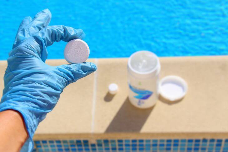 A person wearing protective gloves adding chlorine tablets to pool water to prevent algae coming back